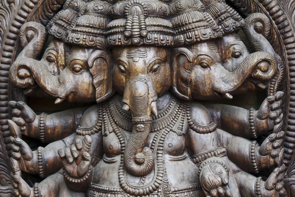 A close photograph of a dark carved-wood Ganesha sculpture with multiple faces and intricate detail