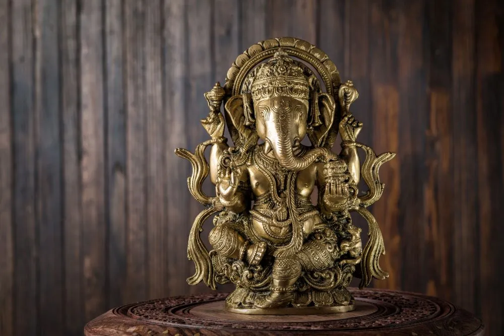A photograph of a brass Ganesha statue standing before weathered dark wooden planks