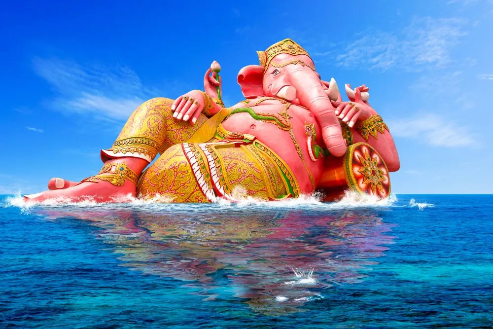 A giant pink reclining Ganesha resting at the edge of a bright blue sea under an open sky