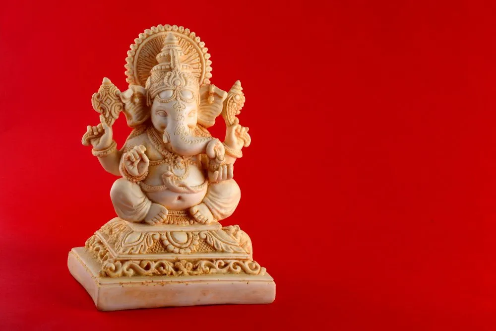 A photograph of a small cream marble-look Ganesha idol on a plain, rich red background