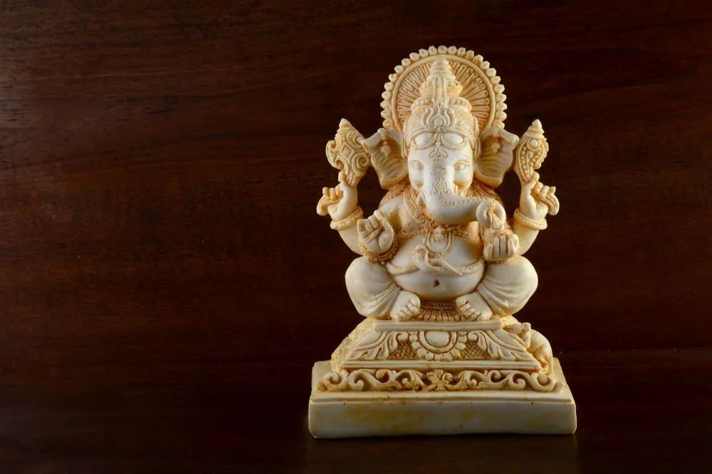 A photograph of a cream marble-look Ganesha idol set against a dark walnut wood background