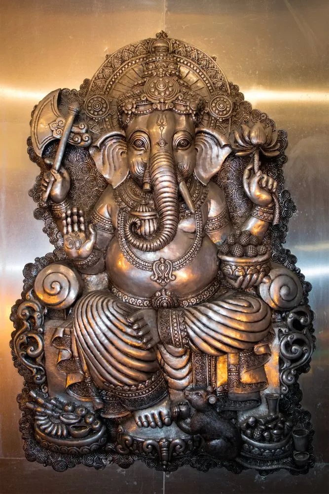 A photograph of an ornate dark-bronze Ganesha statue seated on a carved throne