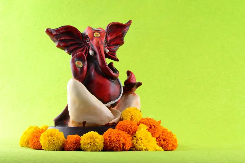 A modern, stylised maroon-and-white Ganesha idol resting on marigolds against bright lime green