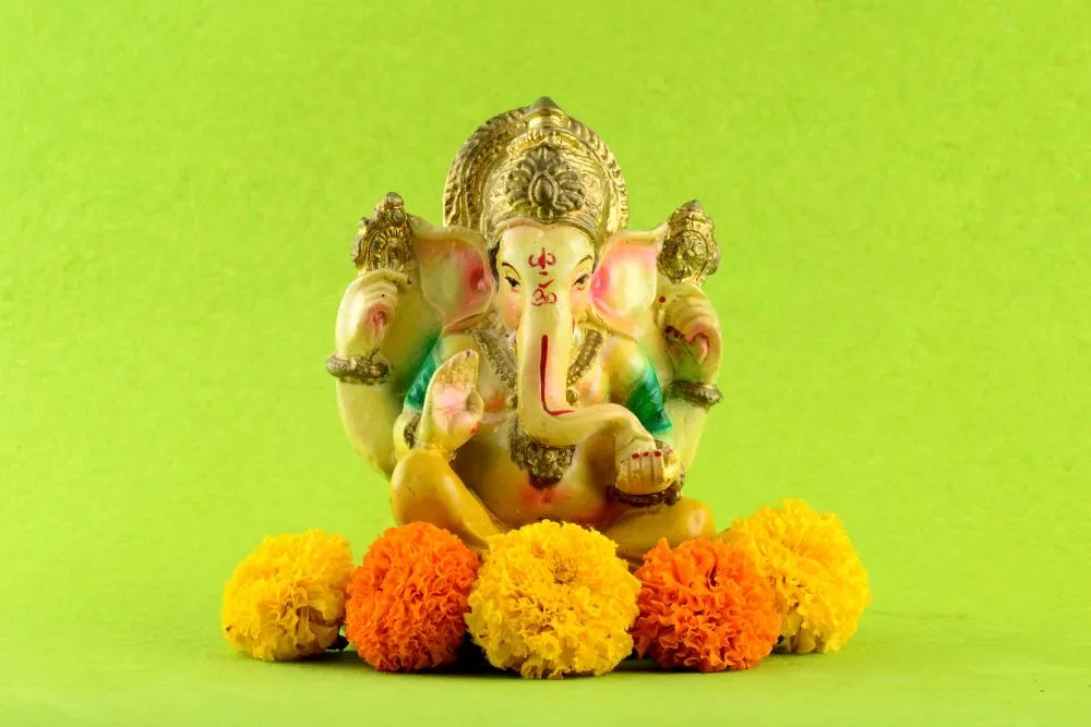 A painted Ganesha idol seated on a bed of marigolds against a bright lime-green background