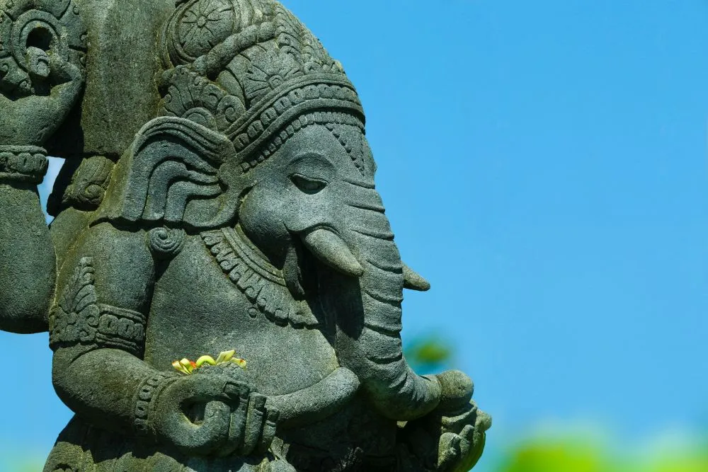 A dark stone Ganesha sculpture seen in profile against a clear blue sky