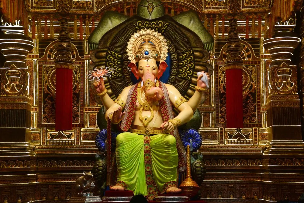 A festival Ganesha idol in green and gold, enthroned before an ornate gilded pandal backdrop
