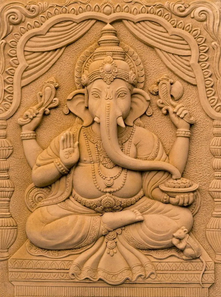 A sandstone-style relief of a seated Ganesha beneath a carved curtain arch, in warm sand tones