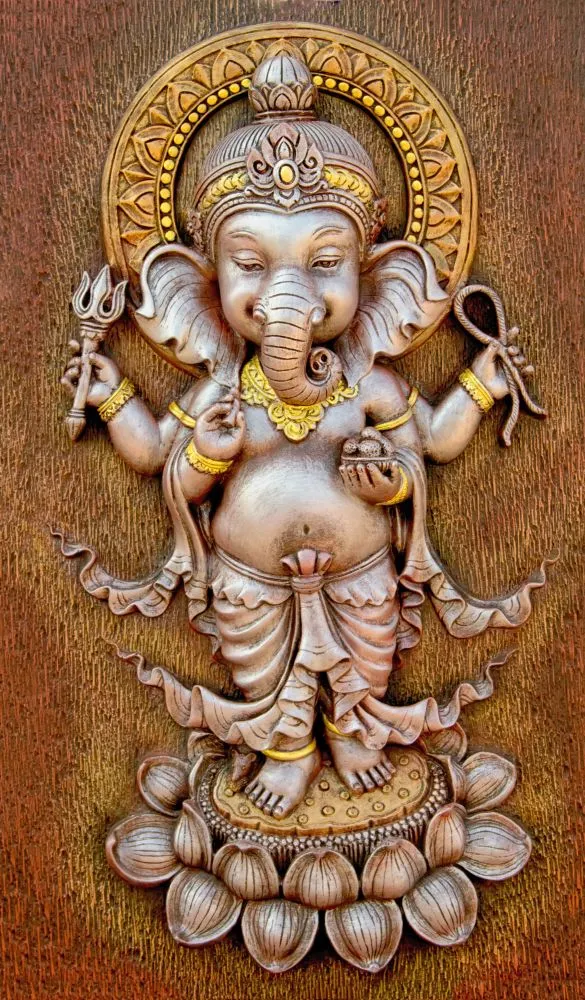 A relief-style dancing Ganesha standing on a lotus, in silver-bronze tones on a textured ochre ground