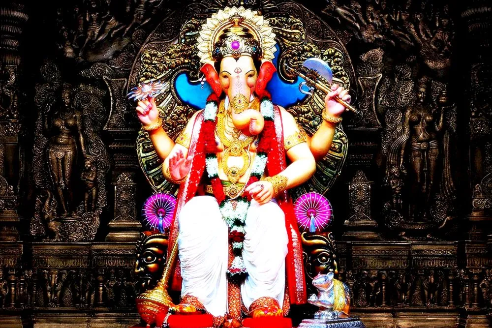 A festival-style Ganesha idol enthroned before a dark, intricately carved temple backdrop