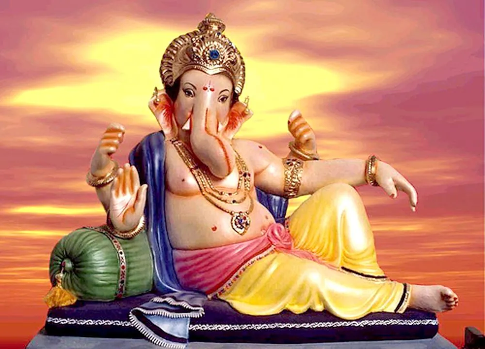 A relaxed Ganesha reclining on a bolster cushion beneath a warm sunset sky
