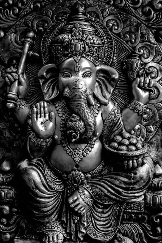 A seated Ganesha in cool silver-grey relief, holding a modak bowl within ornate carved scrollwork
