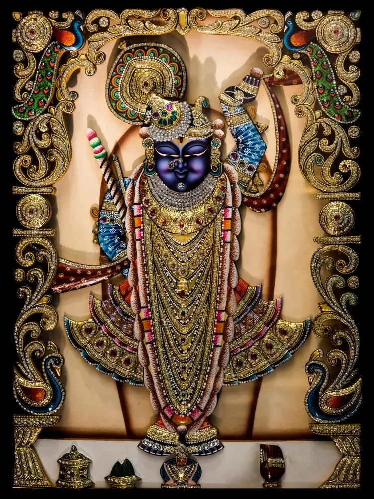 Shrinathji with a deep blue face and long gold-jewelled garments, within an ornate gold border of peacocks and scrolls