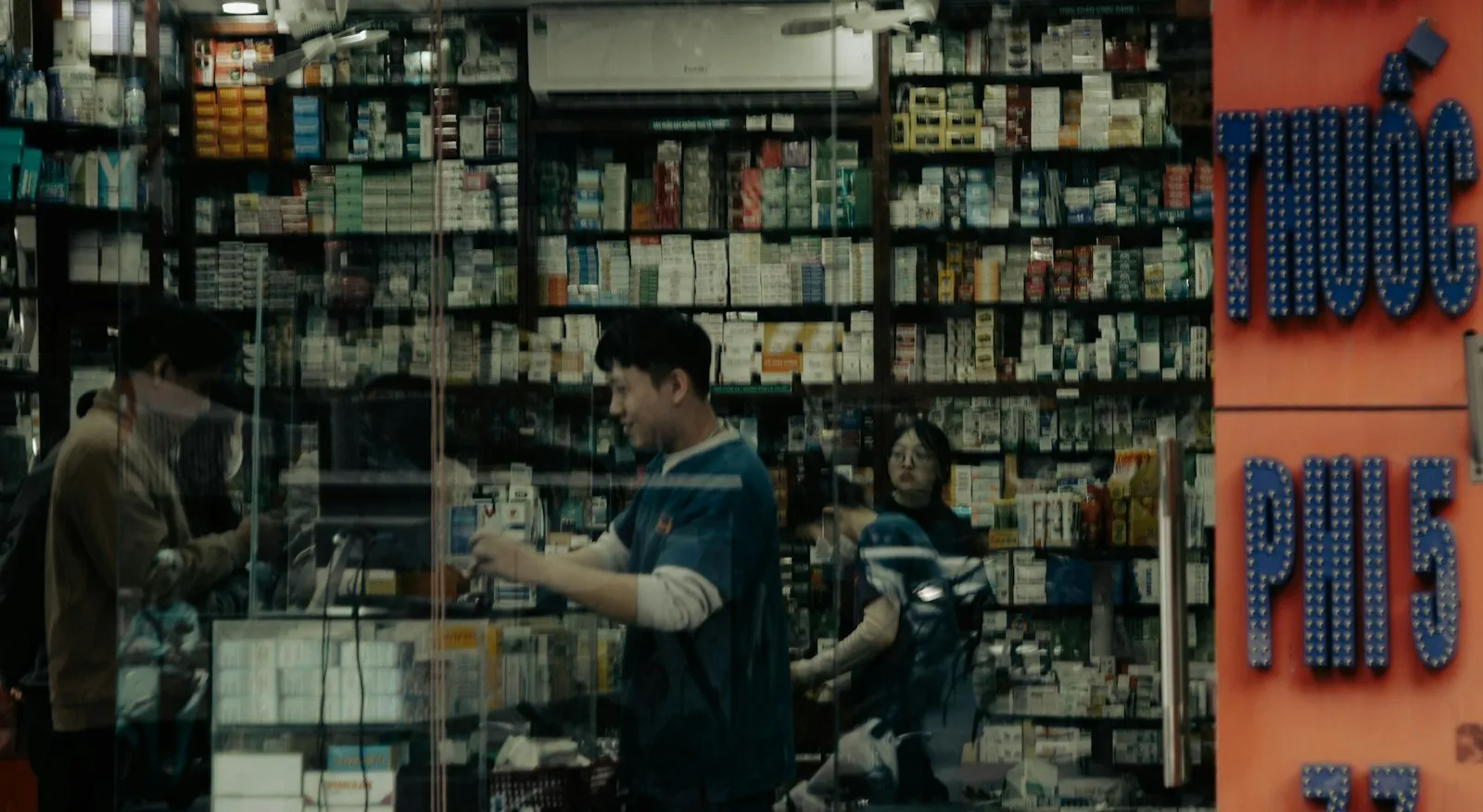 People inside a well-stocked pharmacy with glass doors